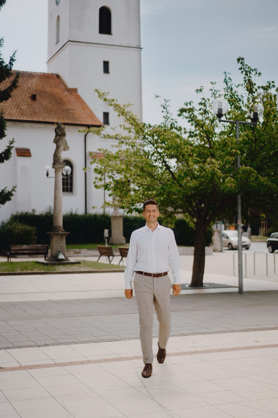 Roman Krištofík kráča po senickom námestí, v pozadí kostol a mariánsky stĺp
